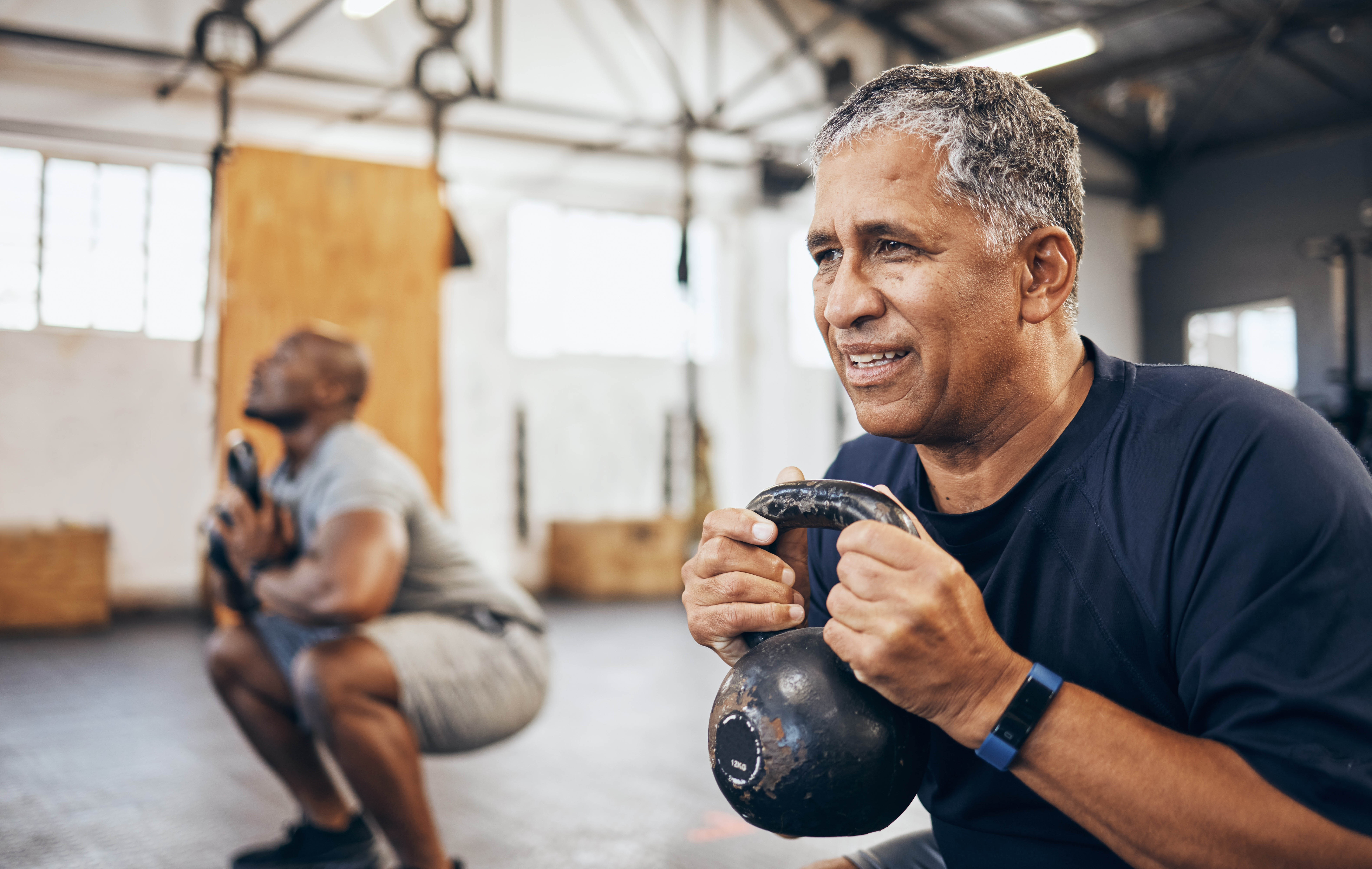 Middle aged man lifting a kettlebell as part of a workout group fitness class in a gym